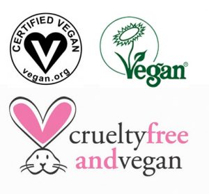 On the top left: the black and white Certified Vegan logo (A black heart with a white v). On the top right: the green Vegan Society trademark with green flower. On the bottom: PETA'S Cruelty Free and Vegan mark with a white bunny. The white bunny has pink ears. 