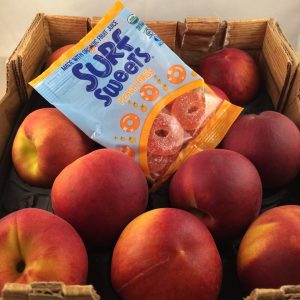 Surf Sweets Organic Peach Rings on top of a box of peaches