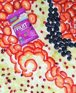 Tasty Brand Organic Fruit Snacks (superfruits) surrounded by strawberries, blueberries, and pomegranate seeds