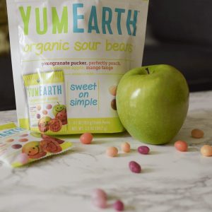 Bag of YumEarth organic sour beans on table. Beans sprinkled on table. Green apple sits by beans.