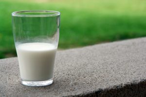 A glass of milk sits on a ledge by a grassy field.