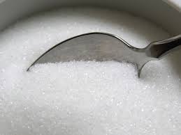 A bowl of sugar with a silver spoon inside.