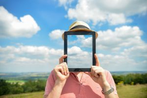 Person outside holds glass tablet with clouds up to face, to represent transparency