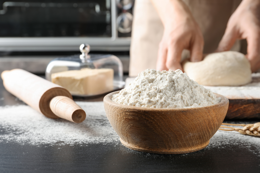 a bowl of flour and a rolling pin with hands in the background making dough