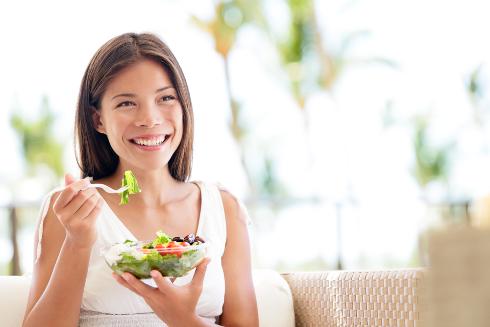 Smiling woman eating salad. Choose which vegan products to sell online.