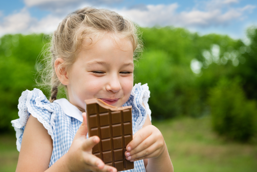 cute girl smiling and eating chocolate outside in summer 