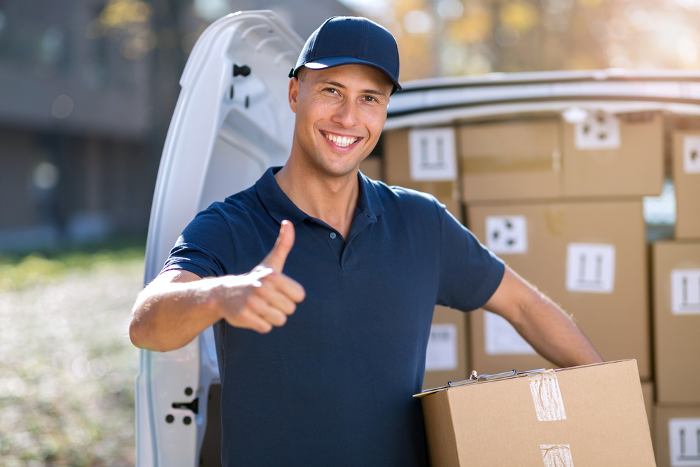 Smiling delivery man giving the thumbs up as he carries a package