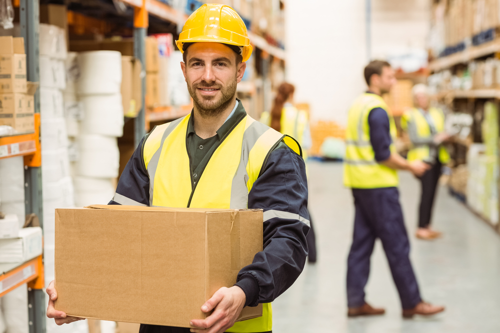 man working in a warehouse carrying a brown box