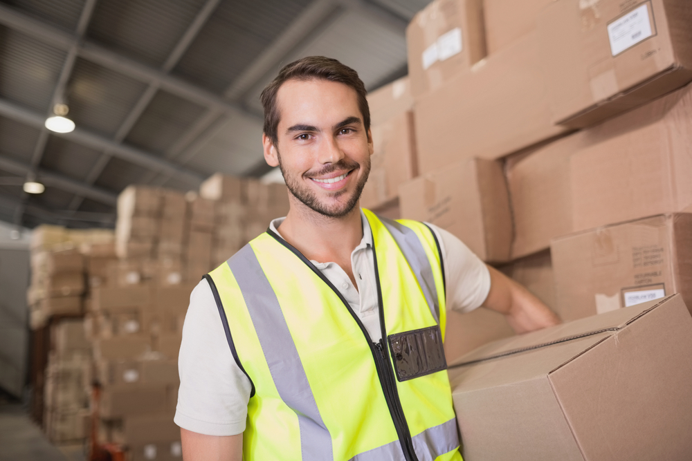 Smiling man working in a wholesale supplier warehouse holding a box