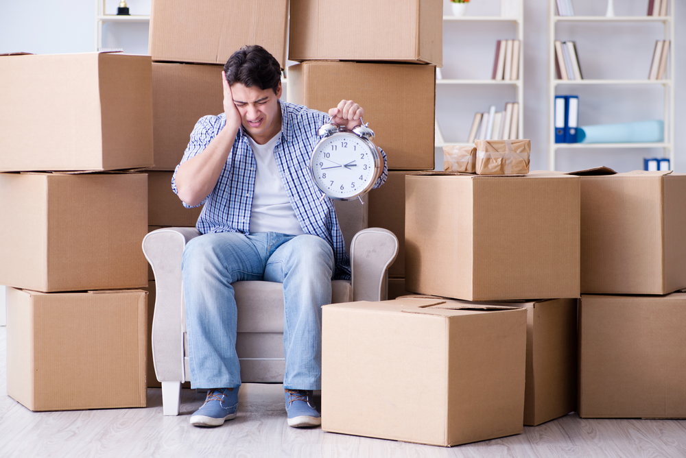 frustrated man holding a clock with packages in the background. Slow shipping times concept