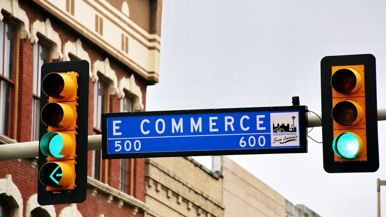 Street sign labeled 'E Commerce' with green traffic lights in the background, indicating a go-ahead for online business.