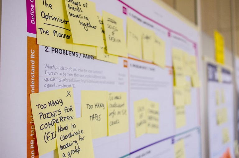 Close-up of a board covered with yellow sticky notes containing handwritten text outlining problems and pain points.
